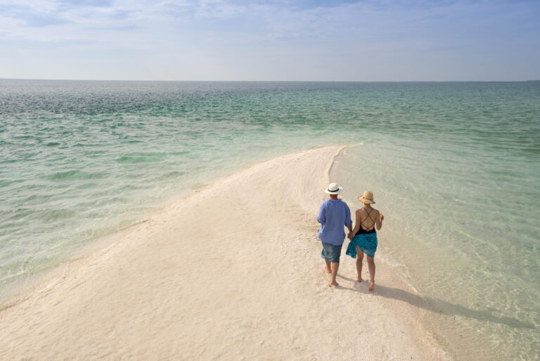 Couple walking hand-in-hand on a sandbar at Benguerra Island